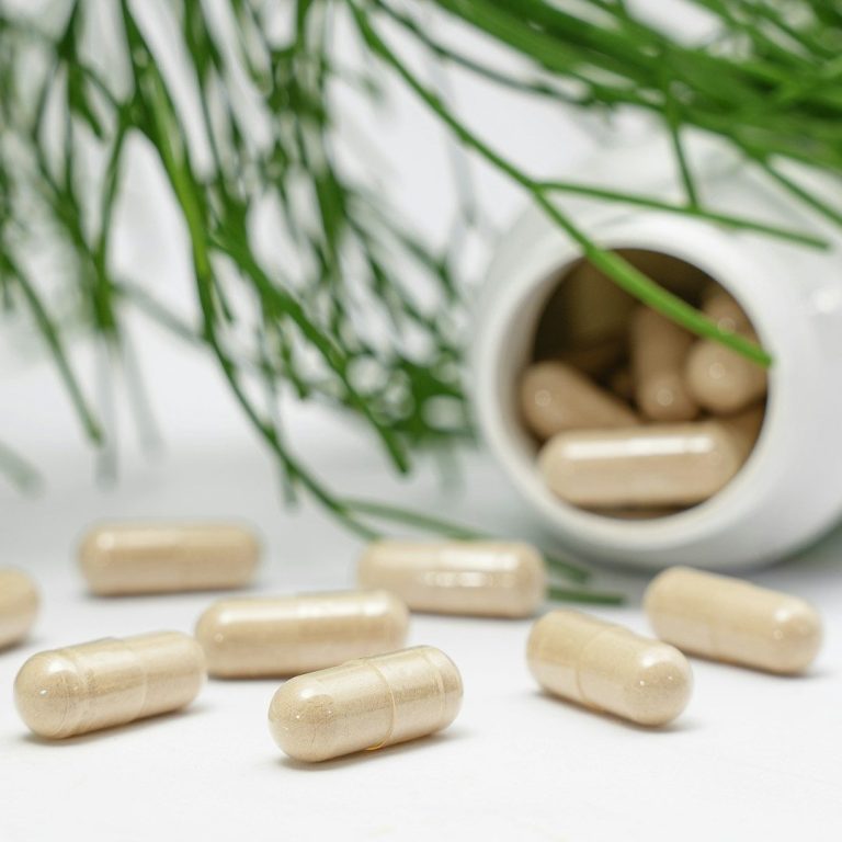 Nahrungsergänzungsmittel liegen verstreut neben einer weißen Schüssel mit weiteren Kapseln.