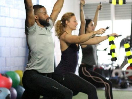 Drei Personen trainieren mit Widerstandsbändern an der Wand in einem Fitnessstudio.