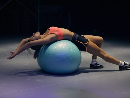 Frau dehnt sich über einen Fitnessball in einer sportlichen Pose.