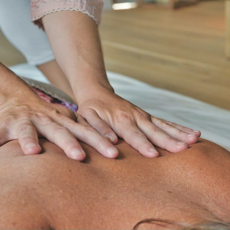 Hände legen sich sanft auf den Rücken einer liegenden Person während einer Massage.