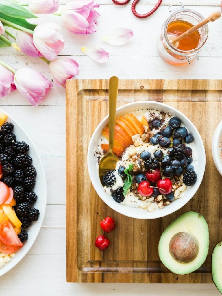 Schüssel mit Joghurt, Obst und Müsli, umgeben von frischen Früchten und Honigglas.